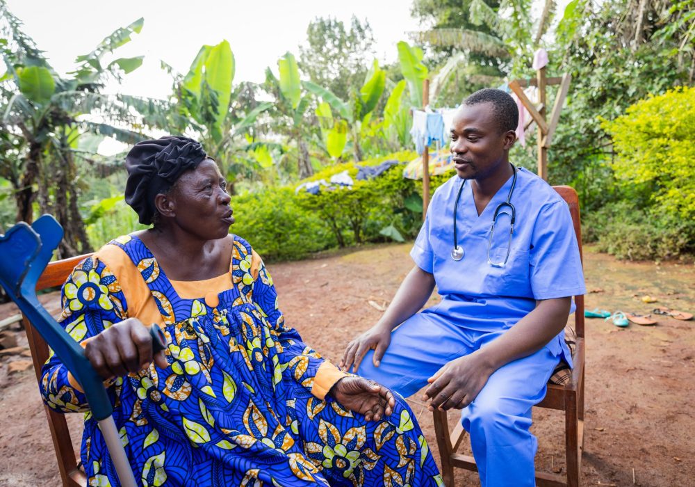 A young African doctor pay a visit to an old ill woman. Home visit to a sick elder